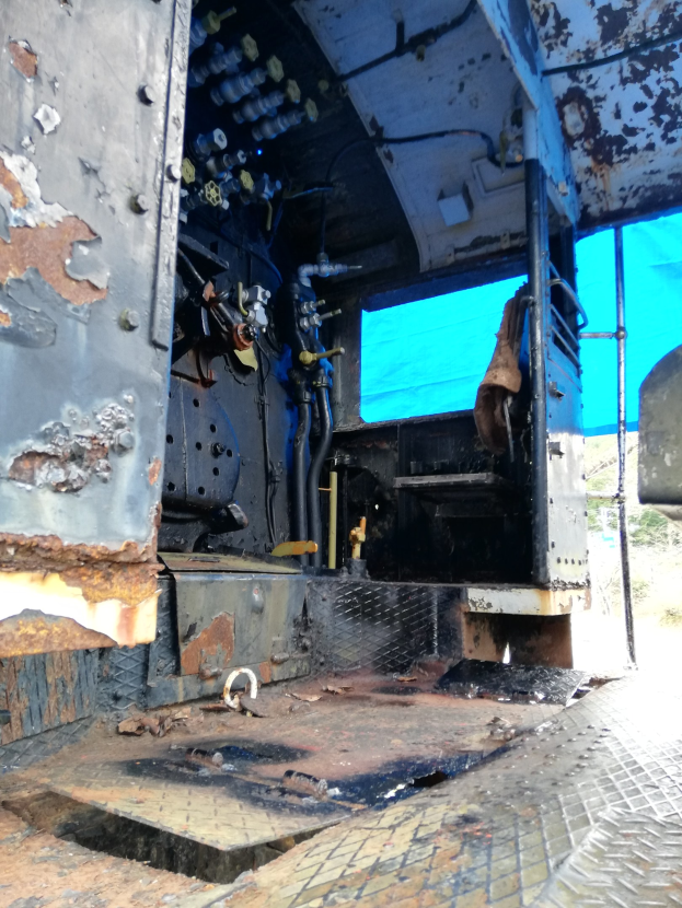 Das Innere einer verrosteten, baufälligen Truck-Kabine mit Bäumen und einem klaren blauen Himmel durch die Windschutzscheibe sichtbar.