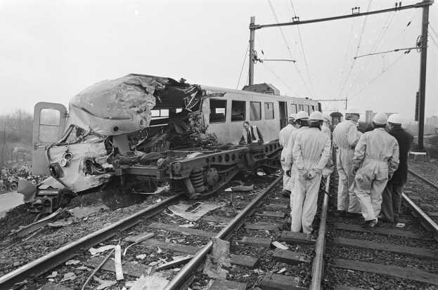 Ein Schwarz-Weiß-Bild einer Zugkollision auf den Gleisen mit Einsatzkräften in Helmen und sichtbarer Infrastruktur.