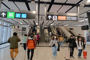 Eine Gruppe von Menschen mit Gepäck geht durch einen Flughafen mit Rolltreppen, Texttafeln, Deckenlampen und Glaswänden im Hintergrund, mit einem Wasserzeichen, das den Flughafen aufgrund der Coronavirus-Pandemie geschlossen anzeigt.