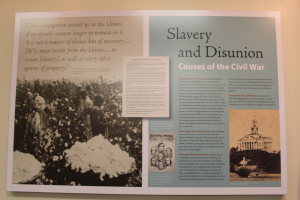 Ein Plakat an einer Wand mit der Aufschrift "Sklaverei und Unionsause des Bürgerkriegs" mit einem Schwarz-Weiß-Bild einer Gruppe von Menschen, die in einer Reihe stehen, im Hintergrund ein Gebäude.