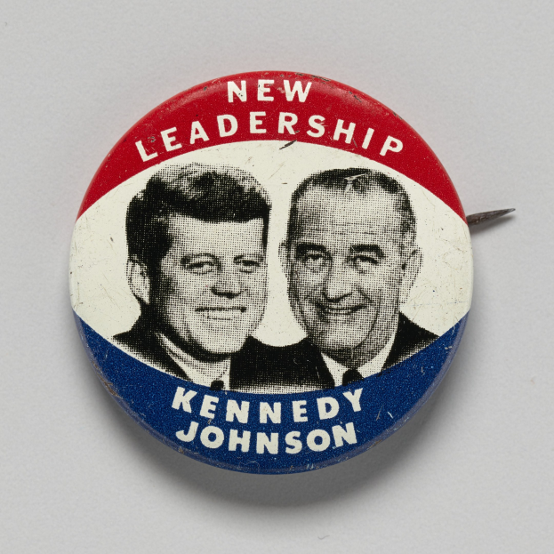 Eine weiße Oberfläche mit einem Ansteckbutton, der zwei Fotos von Kennedy und Johnson zeigt, darunter beschriftet mit "Neue Führung".