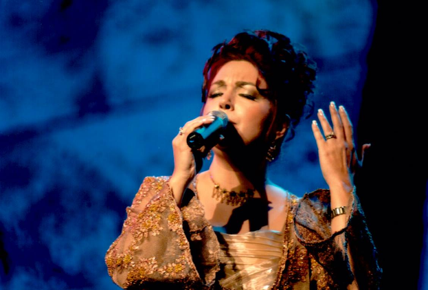 Eine Frau in einem goldenen Kleid singt auf der Bühne der Eurovision Song Contest, mit einem blauen und schwarzen Hintergrund.