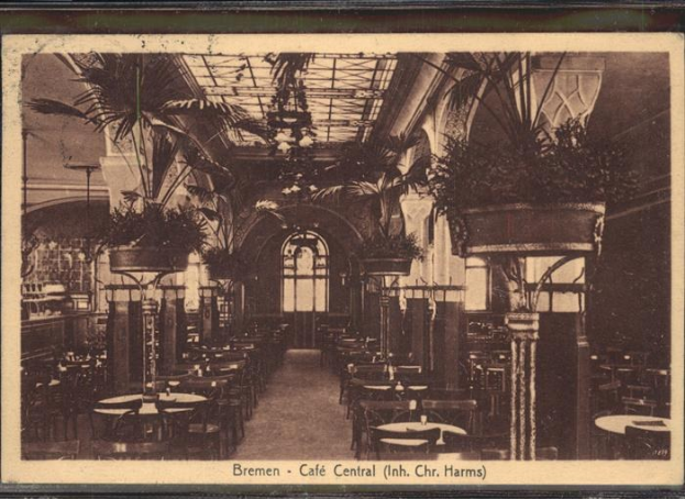 Schwarz-weißes Interieur eines Cafés im Central Hotel, Harms, mit Tischen, Stühlen, hängenden Pflanzen und einem Glasfenster mit Text unten.