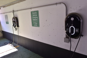 Eine Elektrofahrzeug-Ladestation in einer Tiefgarage mit zwei Ladepunkten an der Wand und Schildern mit Text darauf, der Boden ist unten im Bild zu sehen.