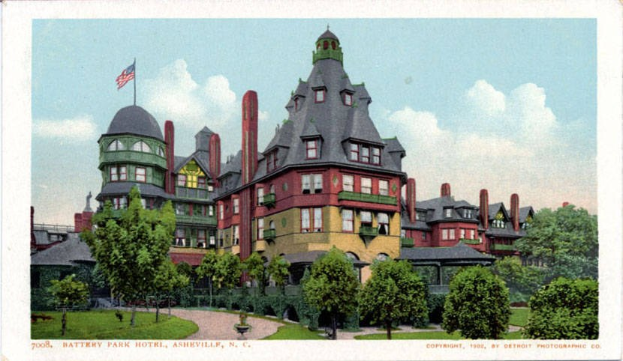 Schwarz-weiß-Postkarte des historischen Battery Park Hotels in Asheville, North Carolina, die das große Gebäude mit einer Fahne auf dem Dach zeigt, umgeben von Grünflächen und einem Weg, mit Himmel im Hintergrund und Text am unteren Rand.