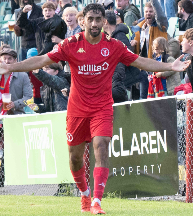Ein Fussballspieler in roter Uniform rennt auf einem Feld mit ausgestreckten Armen, umgeben von Zuschauern im Hintergrund, mit einem "Middlesbrough FC v Swansea City - Sky Bet Championship"-Schild im Hintergrund.