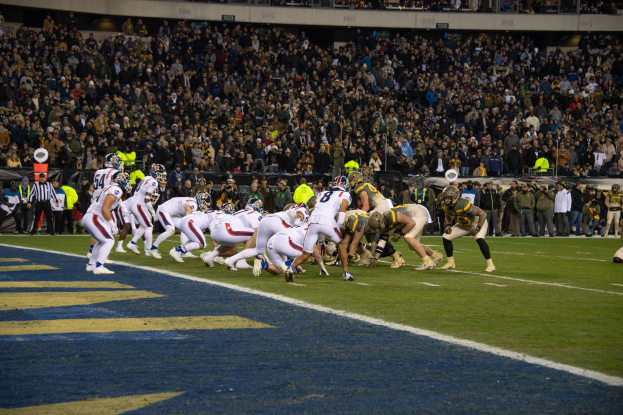 Fussballspieler in Sportkleidung und Helmen auf dem Boden während eines Spiels in einem Stadion mit Zuschauern und Tafeln im Hintergrund.