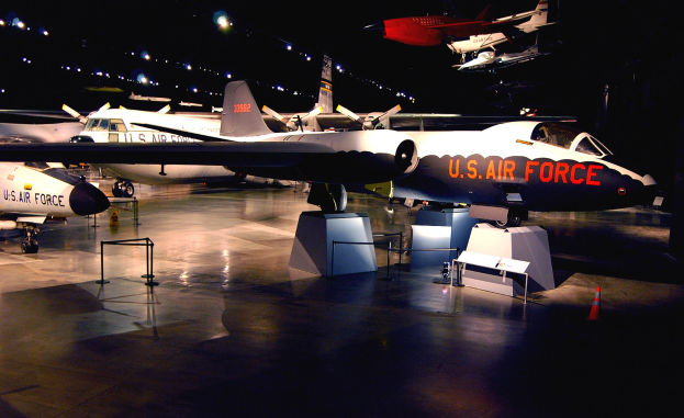 Eine Gruppe von Kampfflugzeugen in einem schwach beleuchteten Museum ausgestellt, umgeben von St├Ąnden, Verkehrskegeln und anderen Bodenobjekten.