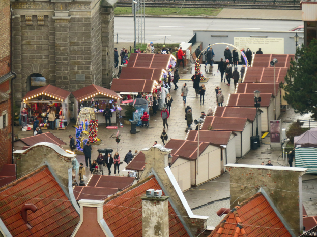 Eine belebte Stadtstraße mit zahlreichen Fußgängern, Gebäuden, Ständen, einem Baum, einem Schild, einer Eisenbahnschiene und einem bewölkten Himmel.