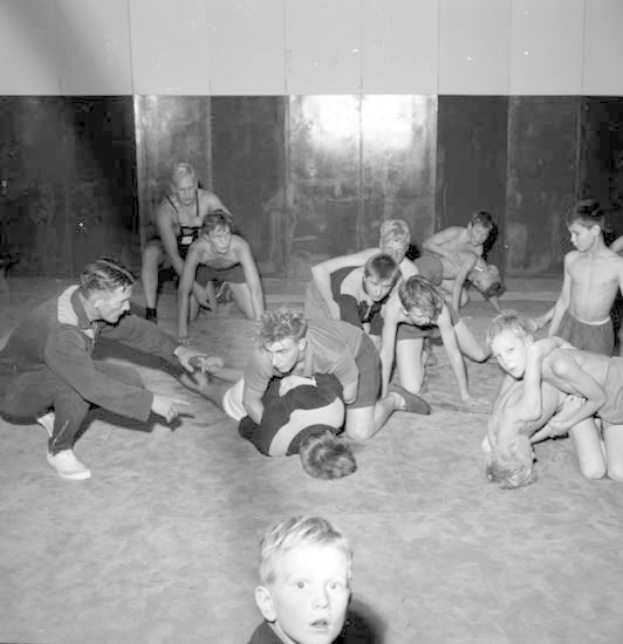 Schwarz-weißes Bild von jungen Jungs, die in einem Gym ringen, mit einer Wand im Hintergrund.