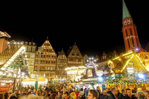 Ein geschäftiger Weihnachtsmarkt in Nürnberg, Deutschland mit Menschen um geschmückte Stände, festliche Lichter und einen Uhrenturm im Hintergrund unter einem dunklen Himmel.