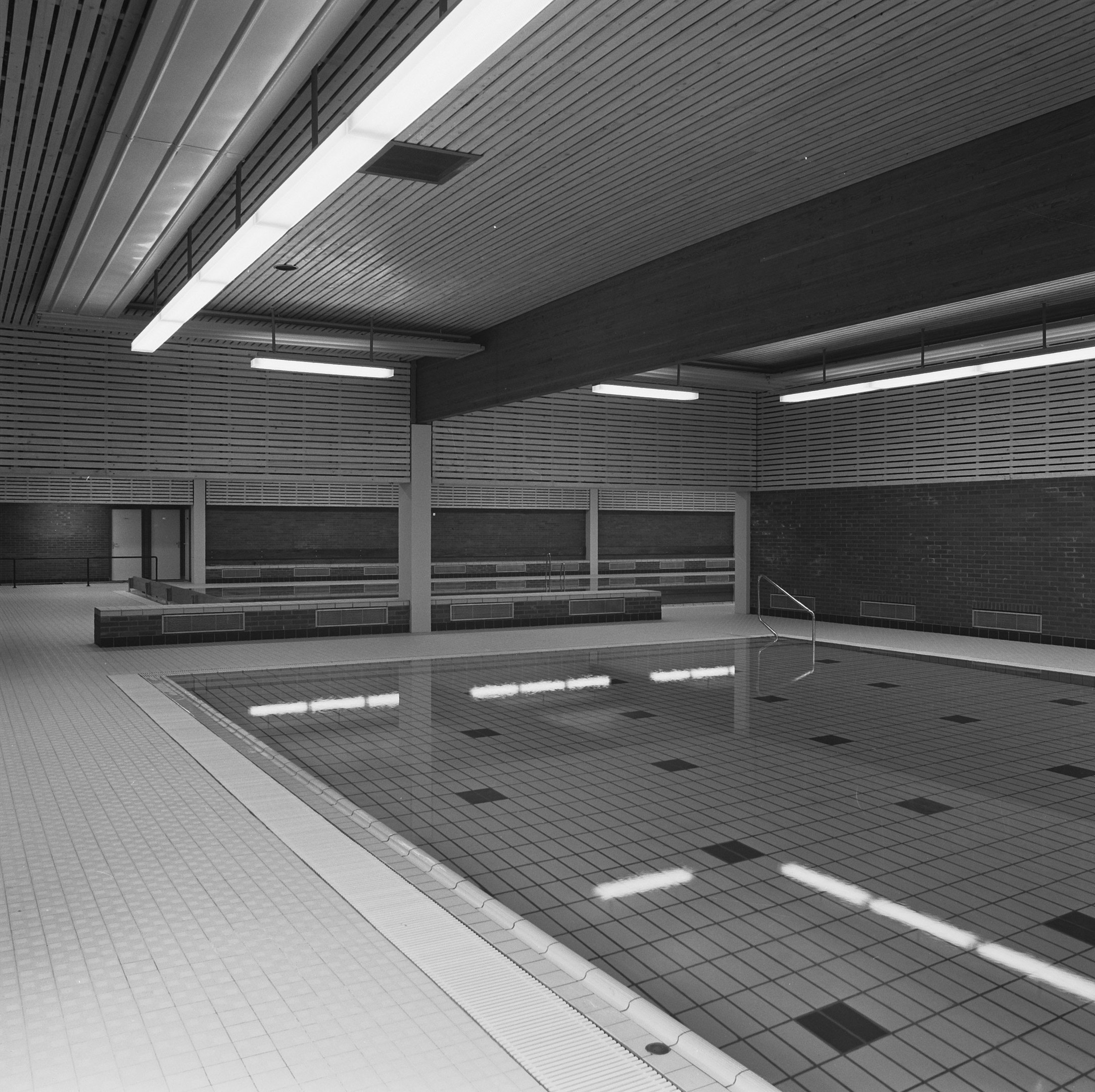 Innenpool mit klarem Wasser, gefliesten Wänden und Boden, Deckenbeleuchtung und minimaler Umgebung in einem großen, ruhigen Raum.