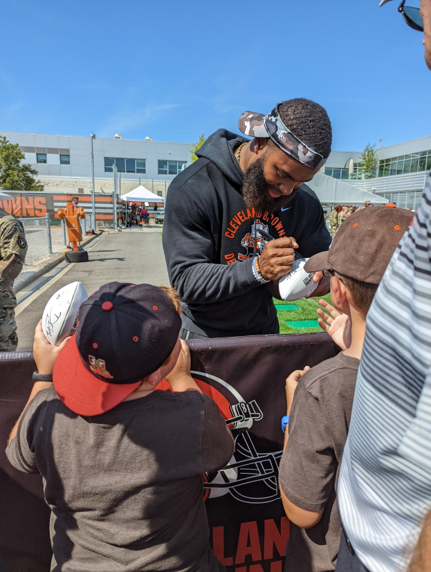 Cleveland Browns Wide Receiver Odell Beckham Jr. signiert Autogramme für Fans mit einer Mütze und Schutzbrille, umgeben von Menschen mit Mützen auf dem Trainingsgelände.