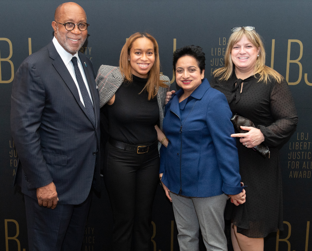 Eine Gruppe von vier Menschen auf einem roten Teppich, die lächeln und für ein Foto posieren, mit einem Schild im Hintergrund, auf dem "Liberty Justice for All Awards" steht.