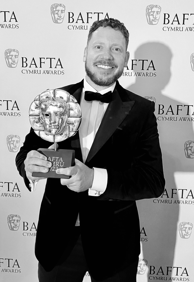 Ein Mann in einem Smoking, der eine BAFTA-Trophäe hält und lächelt, mit einem Hintergrund, auf dem "BAFTA Awards 2018" steht