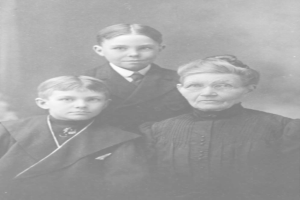 Ein Schwarz-Weiß-Foto einer Frau und zweier Jungen, die posieren, wobei die Frau eine Brille trägt und der Hintergrund unscharf ist.