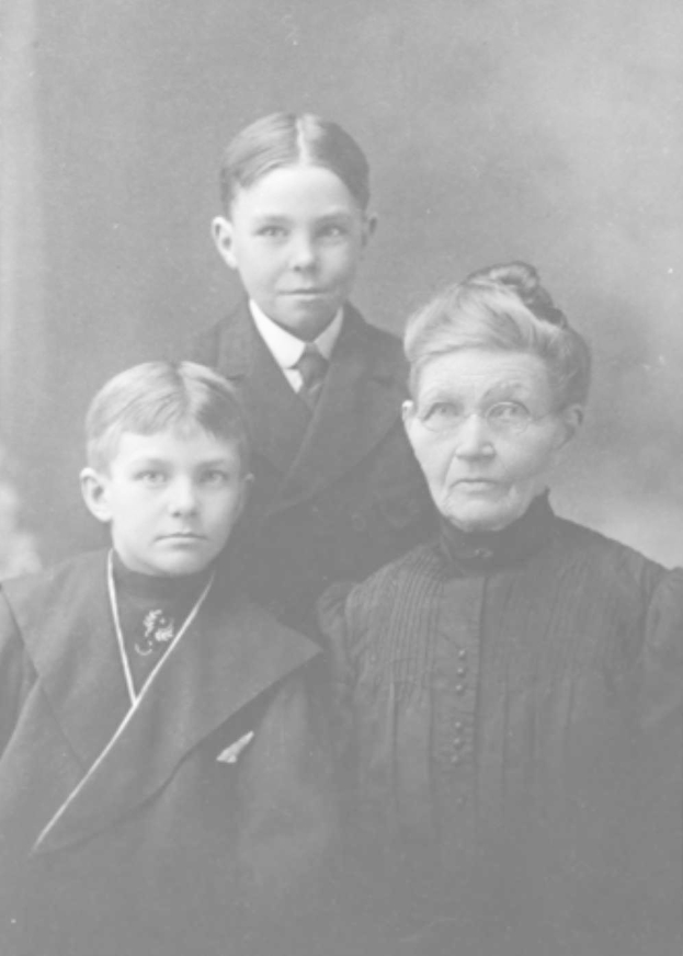 Ein Schwarz-Weiß-Foto einer Frau und zweier Jungen, die posieren, wobei die Frau eine Brille trägt und der Hintergrund unscharf ist.