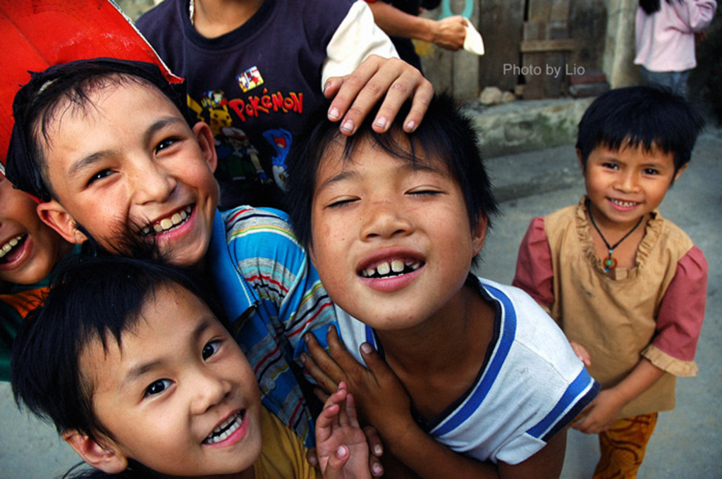 Kinder, die mit einem Grinsen auf der Straße und vor einer Wand stehen.