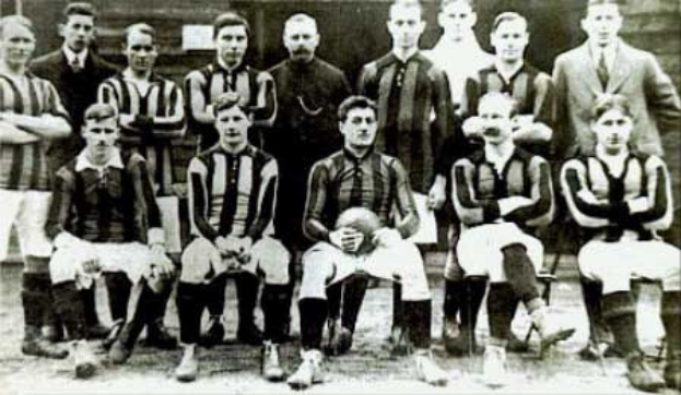 Schwarzes und weißes Foto einer Fußballmannschaft, einige stehen, einige sitzen, vor einer Wand mit "Ballymena Football Club"-Text unten.