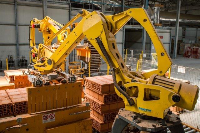 Großes Industriegelände mit gestapelten Kisten, Kränen, Zaun, Pfählen und einer fernen Wand in einer Fertigungsumgebung.