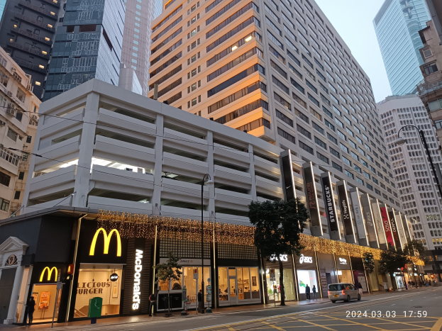 Ein McDonald's-Restaurant auf einer belebten Stadtstraße mit hohen Gebäuden, Fahrzeugen, Fußgängern, Straßenmöblierung, Bäumen und einem klaren Himmel.