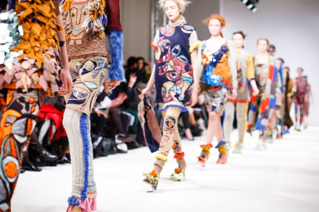 Eine Gruppe Von Frauen, Die Auf Einem Laufsteg In London Fashion Week Gehen, Mit Einer Zuschauermenge Im Hintergrund Unter Hellen Lichtern.