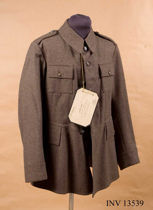 WWII-Deutsches-Luftwaffen-Offiziersjacke mit angebrachtem Anhänger, der auf einer Schaufensterpuppe gegen einen cremefarbenen Hintergrund gestellt ist, mit Text unten.