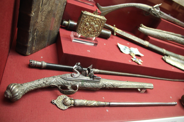 Vitrine mit verschiedenen Waffen, darunter ein Steinschlossgewehr, ordentlich auf einem roten Tisch arrangiert.