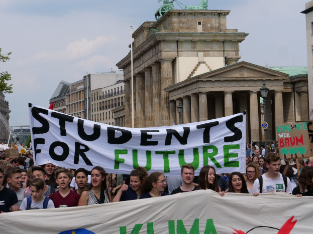 Eine Gruppe von Schülern marschiert in Berlin mit einer bunt bemalten "Students for Future"-Tafel durch die Straßen.