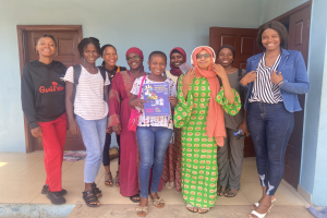 Eine Gruppe von Frauen, die strahlen und Bücher in der Hand halten, vor einem Schulgebäude in Nigeria, mit einem Tuch auf dem Boden dahinter.