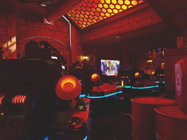 Ein hell erleuchteter Raum voller verschiedener Arcade-Videospielautomaten, Bildschirme und Gegenstände, darunter eine sichtbare Leitung und Deckenlampen.