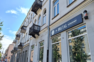 Ein Friseurladen in Berlin mit Gebäuden, Bäumen, Laternen und Passanten unter einem bewölkten Himmel.