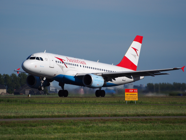 Airbus A320-200 der Austrian Airlines startet von Frankfurt Airport, mit einem Schild im Vordergrund, Gras, Bäumen, Gebäuden und einem klaren blauen Himmel im Hintergrund.