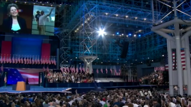 Eine große Menschenmenge sitzt vor einer Bühne mit einem Podium, Mikrofon, Flaggen, einem Bildschirm und Beleuchtungsausrüstung und wartet auf eine Präsidentschaftsdiskussion.