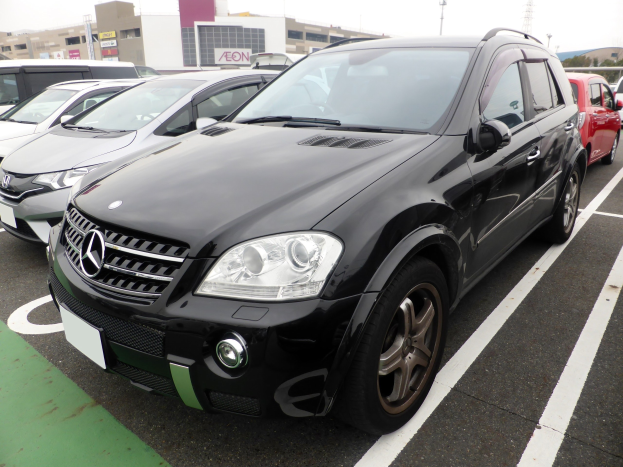 Schwarzer Mercedes-Benz ML 350 CDI BlueEfficiency auf einem Parkplatz mit Gebäuden, Masten, Bäumen und einem klaren blauen Himmel im Hintergrund.