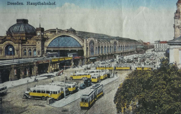 Eine sepiafarbene Postkarte des Dresdner Hauptbahnhof Bahnhofs in Deutschland, die eine belebte Straßen Szene mit Fahrzeugen, Fußgängern, Bäumen, Gebäuden und einem bewölkten Himmel zeigt.