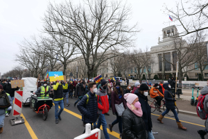 Ein große Protestmarsch mit Menschen, die eine Straße in Washington, D.C. entlanggehen, einige halten Schilder und andere fahren Fahrräder, mit Bäumen und einem klaren blauen Himmel im Hintergrund.