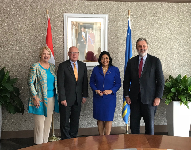 Eine Gruppe strahlender Menschen, die um einen Tisch mit Papieren stehen, umgeben von Fahnen, Topfpflanzen und einem Foto auf der Wand, feiern die Unterzeichnung eines Memorandums zwischen den Vereinigten Staaten und Kanada.