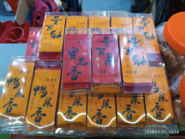 Ein Tisch mit verschiedenen verpackten Lebensmitteln und Gegenständen, im Hintergrund steht eine Person während eines chinesischen Neujahrsfests.