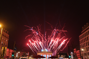 Eine belebte Stadtstraße am Silvesterabend in Berlin, voller Menschen, Fahrzeuge und Gebäude, beleuchtet von Lichtern und Feuerwerk am Himmel.