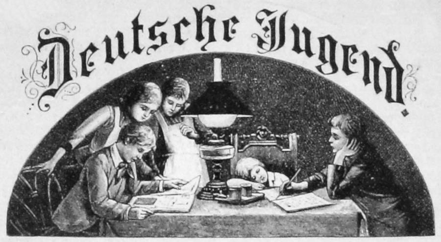 Eine Gruppe von Kindern sitzt um einen Tisch mit einer Lampe, Büchern und anderen Gegenständen. Über ihnen hängt ein schwarz-weißes Plakat mit der Aufschrift "Deutsche Jugend".