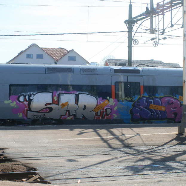 Graffiti ist auf der Seite eines Zuges mit Kabeln im Vordergrund und Häusern mit Fenstern im Hintergrund zu sehen.