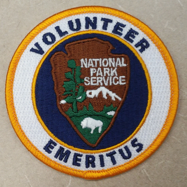Runder Patch mit "Freiwilliger Nationalparkdienst Emeritus" in schwarzer Schrift auf einem weißen Hintergrund, umrandet von einem blauen Rand und einem gelben Kreis.