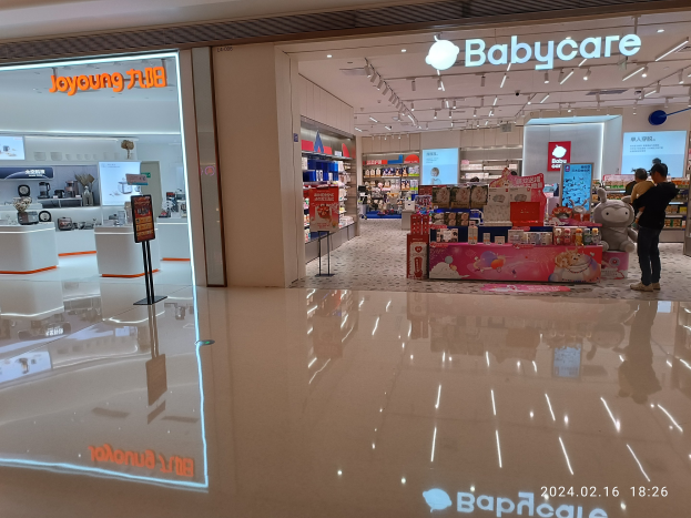 Laden für Babypflege im Mall of Asia mit Regalen voller Gegenstände, Schildern, einem Bildschirm, Deckenleuchten und einer Gruppe von Menschen umgeben von Spielzeugen.