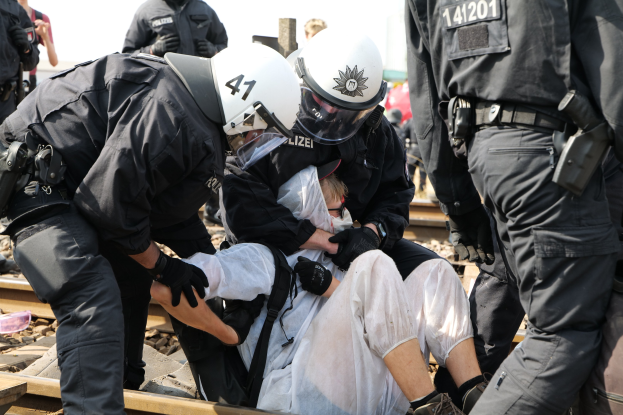 Polizeibeamte in Einsatzausrüstung nehmen einen Mann in einem weißen Kleid auf einem Bahngleis fest.