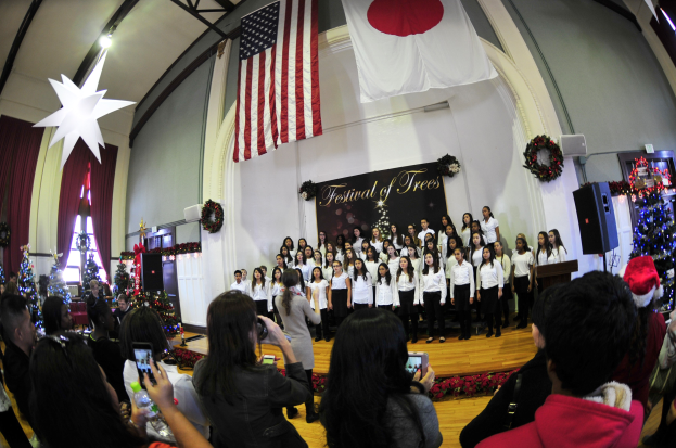 Menschen auf einer Bühne mit Weihnachtsdekoration, einem Podium und einer Menge darunter mit Kameras und Handys.