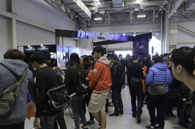 Eine Gruppe von Menschen steht vor einer Menge auf einer Gaming-Messe, mit Schildern, Lichtern und Rohren im Hintergrund.