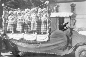 Schwarzes und weißes Bild einer Gruppe von Frauen auf einem Truck, die Körbe halten, mit einem Gebäude und Bäumen im Hintergrund.