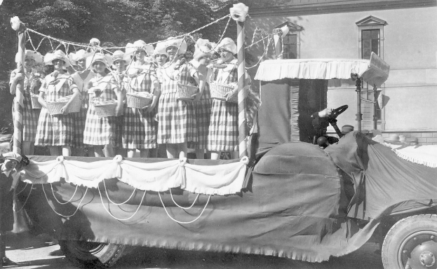 Schwarzes und weißes Bild einer Gruppe von Frauen auf einem Truck, die Körbe halten, mit einem Gebäude und Bäumen im Hintergrund.