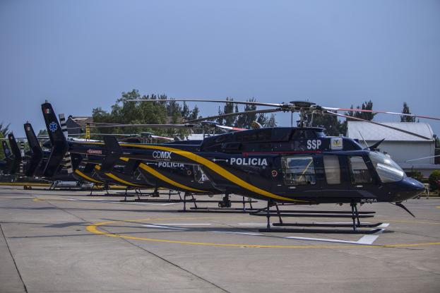 Polizeihubschrauber auf einem Flughafenparkplatz mit umliegenden Gebäuden, Bäumen und einem klaren blauen Himmel.
